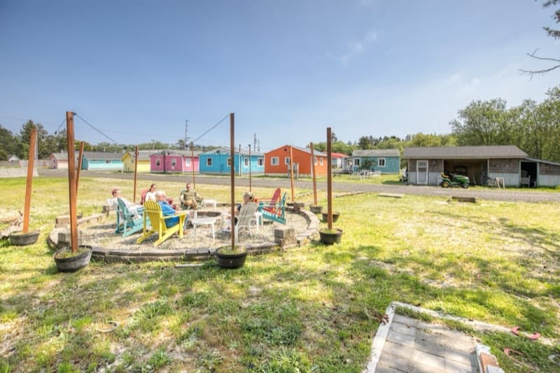 Guests gathered around the fire pit with colorful cottages in the background